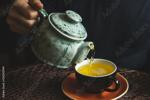 man pours tea from a teapot in a tea Cup