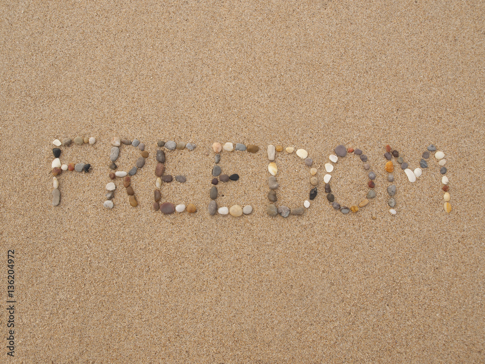 word freedom written with stones and shells on the beach by the ocean word freedom written with stones and shells on the beach by the ocean