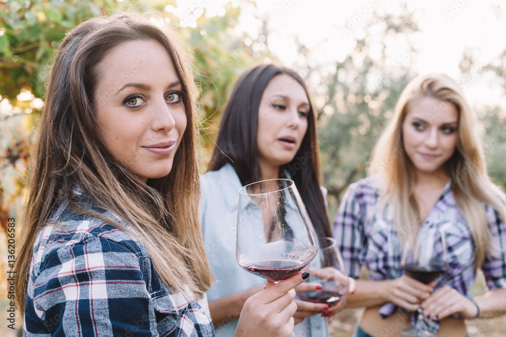 Three young female friends drinking wine in vineyard at sunset Three young female friends drinking wine in vineyard at sunset