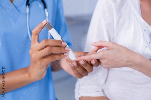 Mid section of doctor examining pregnant woman's blood sugar