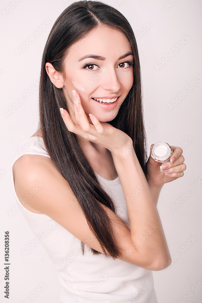 Applying cosmetic cream. A beautiful young woman applying face moisturizer. Scine care of the face and hands