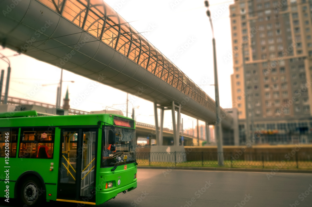 green trolleybus rides on the road in city. against the backdrop of high-rise buildings and on top pedestrian