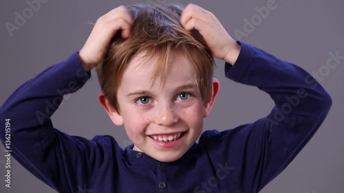 smiling adorable little boy with freckles scratching his red hair