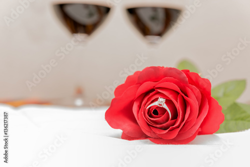 Diamond ring inside red rose over two wine glasses