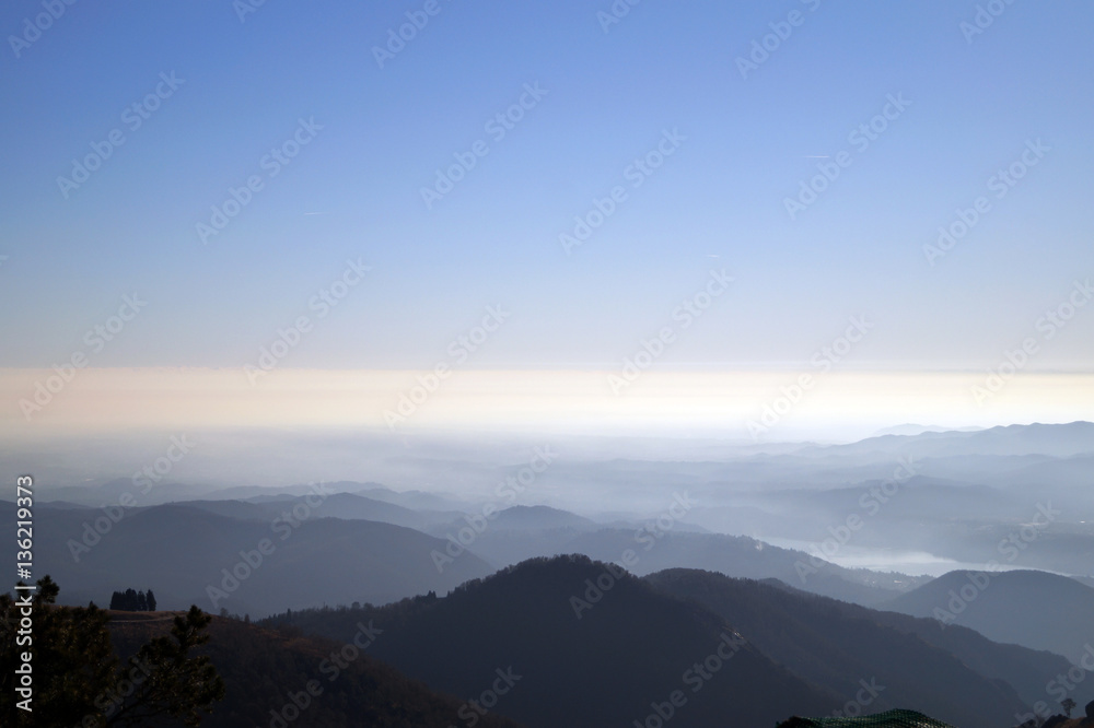 Vista aerea paesaggio di montagna con lago d'orta sullo sfondo e foschia sotto cielo azzurro 