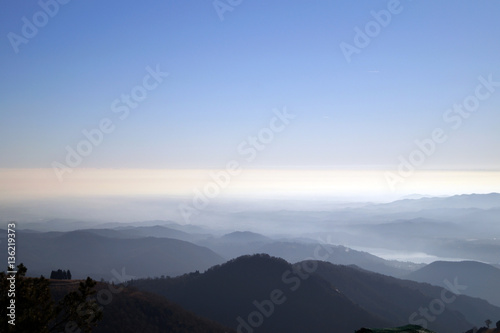 Vista aerea paesaggio di montagna con lago d'orta sullo sfondo e foschia sotto cielo azzurro 