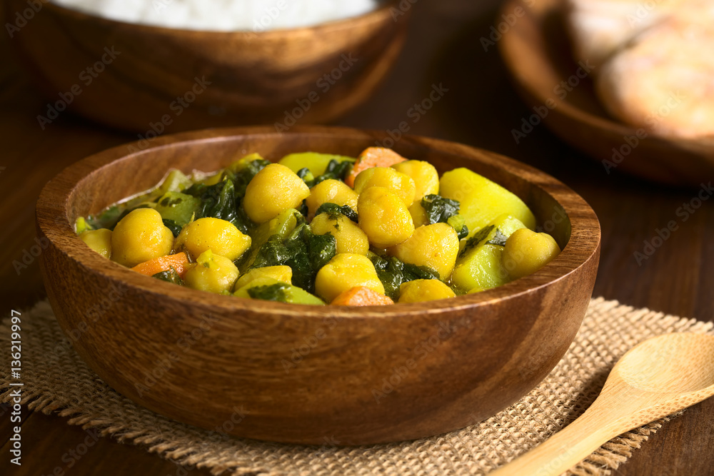 Vegan chickpea curry or chana masala with spinach, potato and carrot served in wooden bowl, photographed with natural light (Selective Focus, Focus one third into the curry)