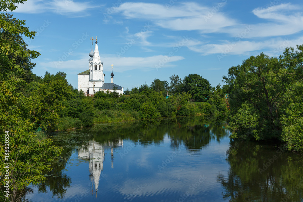 Landscape with green trees, river, blue sky and white church on a hill in Suzdal, Russia Landscape with green trees, river, blue sky and white church on a hill in Suzdal, Russia