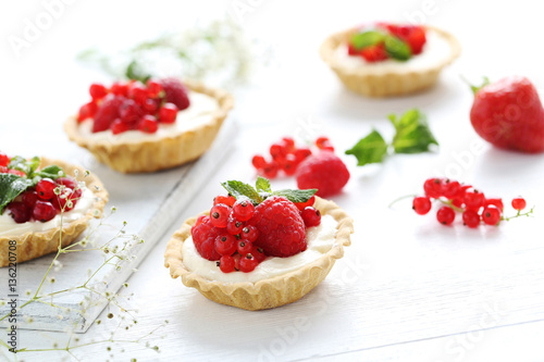 Dessert tartlets with berries on white wooden background