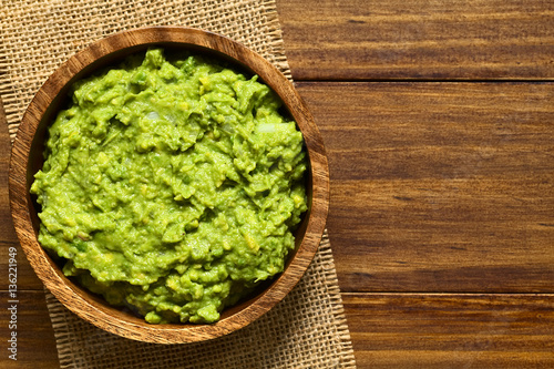Avocado dip or guacamole in wooden bowl, photographed overhead with natural light (Selective Focus, Focus on the avocado dip)