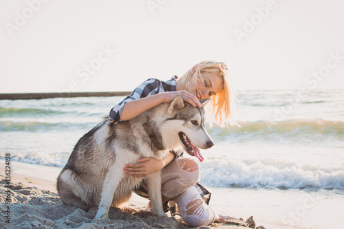 Young female hugging with siberian husky dog on the beach at sunrise photo