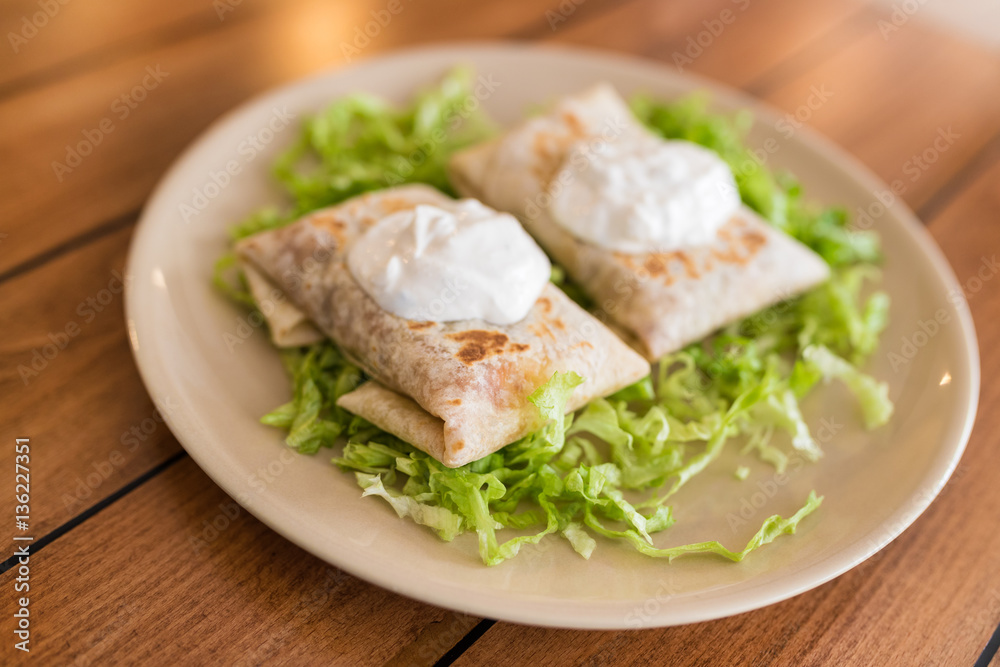Chimichangas on salad with cream on top.