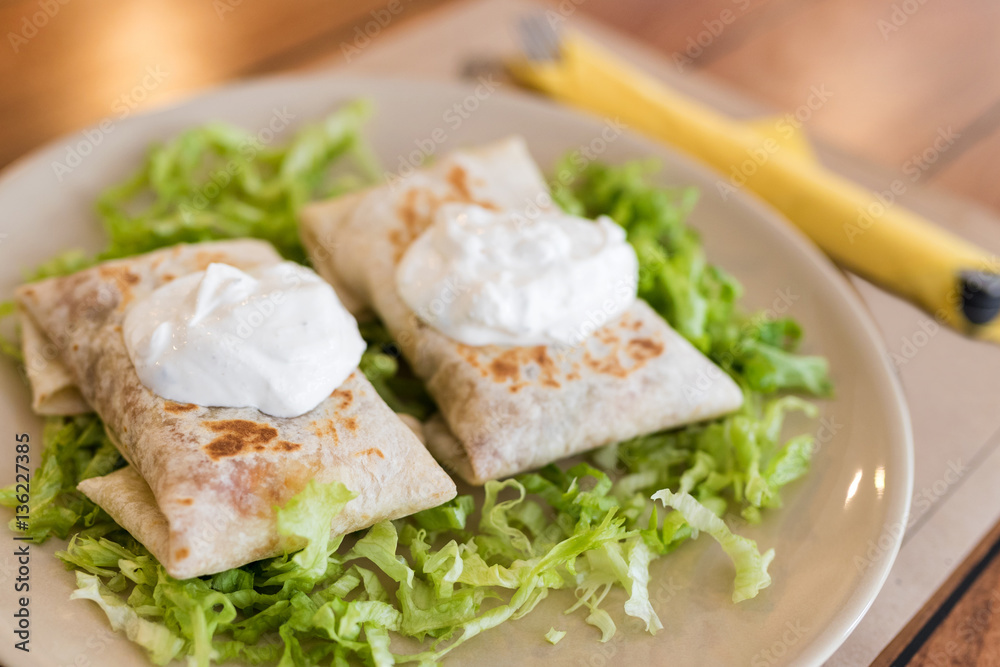 Chimichangas on salad with cream on top.