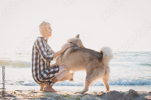 Young female playing with siberian husky dog on the beach at sunrise