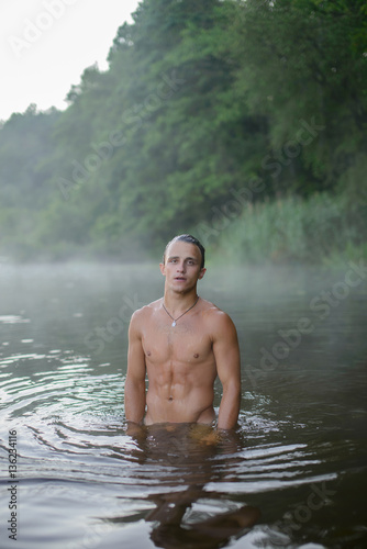 cute sexy athletic guy without underwear is standing in the river, morning, dawn