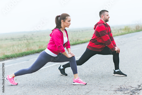 Young fitness couple stretching muscles before running on open road.