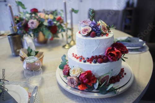 A large two-tiered cake decorated with fruit and fresh flowers. The composition of flowers, fruits and berries. Trendy wedding cake.