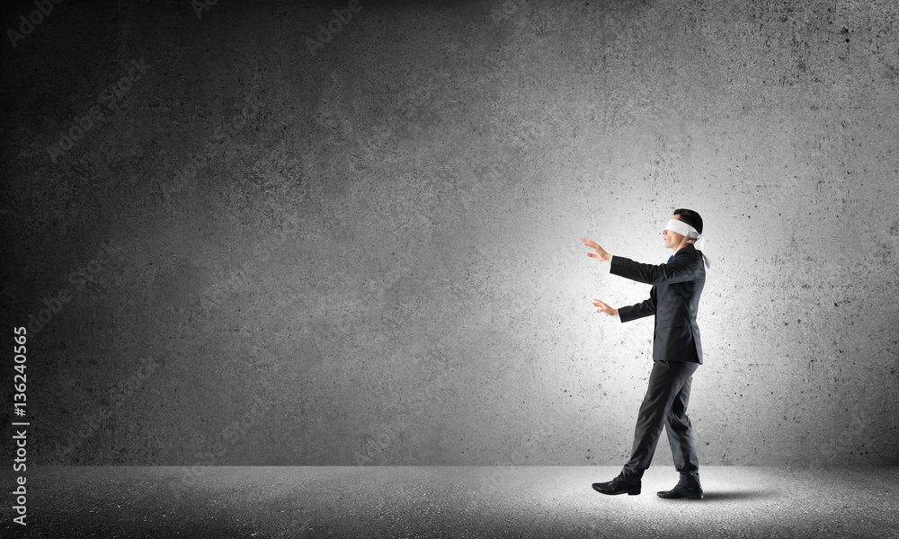 Business concept of risk with businessman wearing blindfold in empty concrete room Business concept of risk with businessman wearing blindfold in empty concrete room