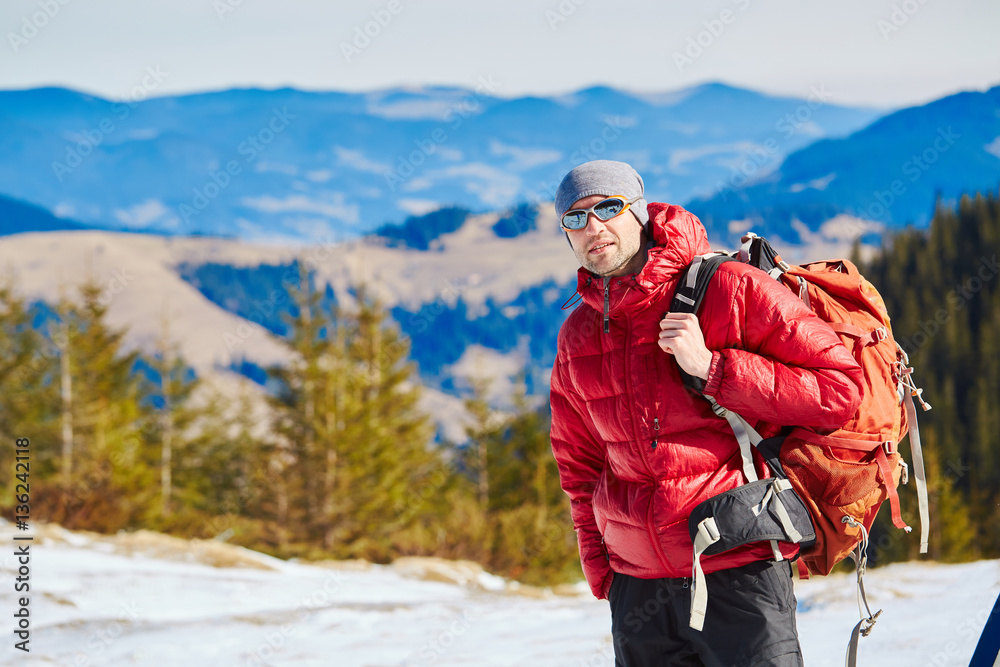 hiker in red down jacket with backpack near the tent in the Carpathians mountains at winter