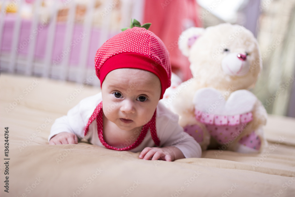 Close up of a beautiful baby girl lying on the bed. Infant lying on a bed. Family morning at home. Happy baby wearing strawberry shirt and pants. Newborn kid with toy bear. Close up of a beautiful baby girl lying on the bed. Infant lying on a bed. Family morning at home. Happy baby wearing strawberry shirt and pants. Newborn kid with toy bear.