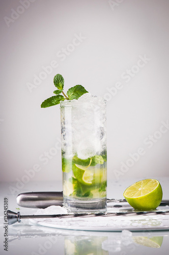 Glass of mojito cocktail with knife, half of a lime and ice on t