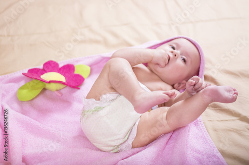 Happy baby wearing pink bathrobe lying on parents bed after bath or shower. Clean dry child in the bedroom. Bathing and washing of little kids. Children hygiene. Textile for infants.