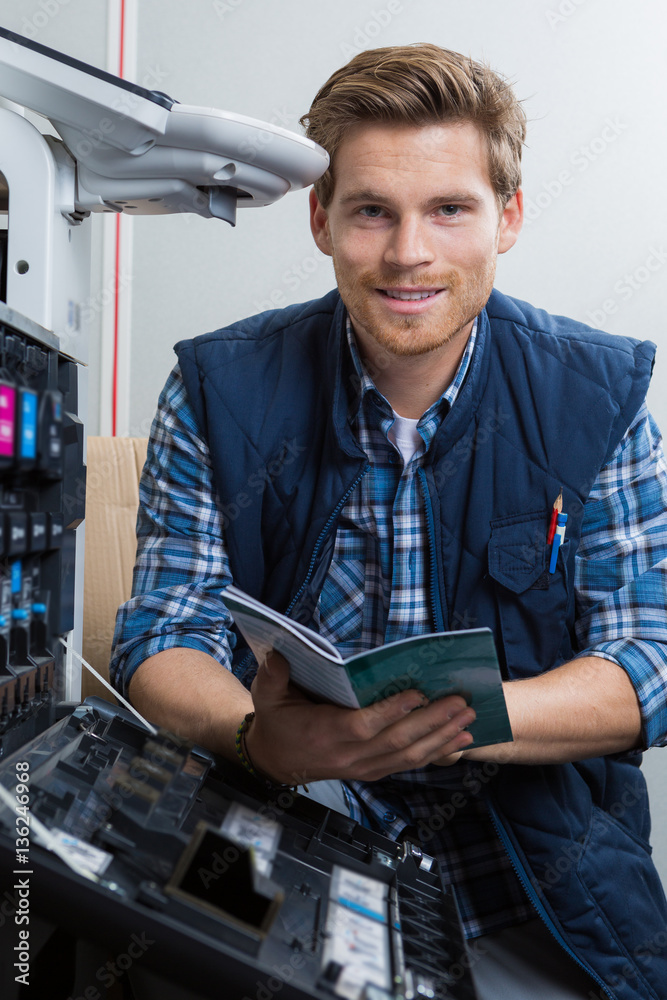 Man repairing photocopier holding manual foto de Stock Adobe Stock