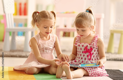 Cheerful little girls with book sitting on the floor