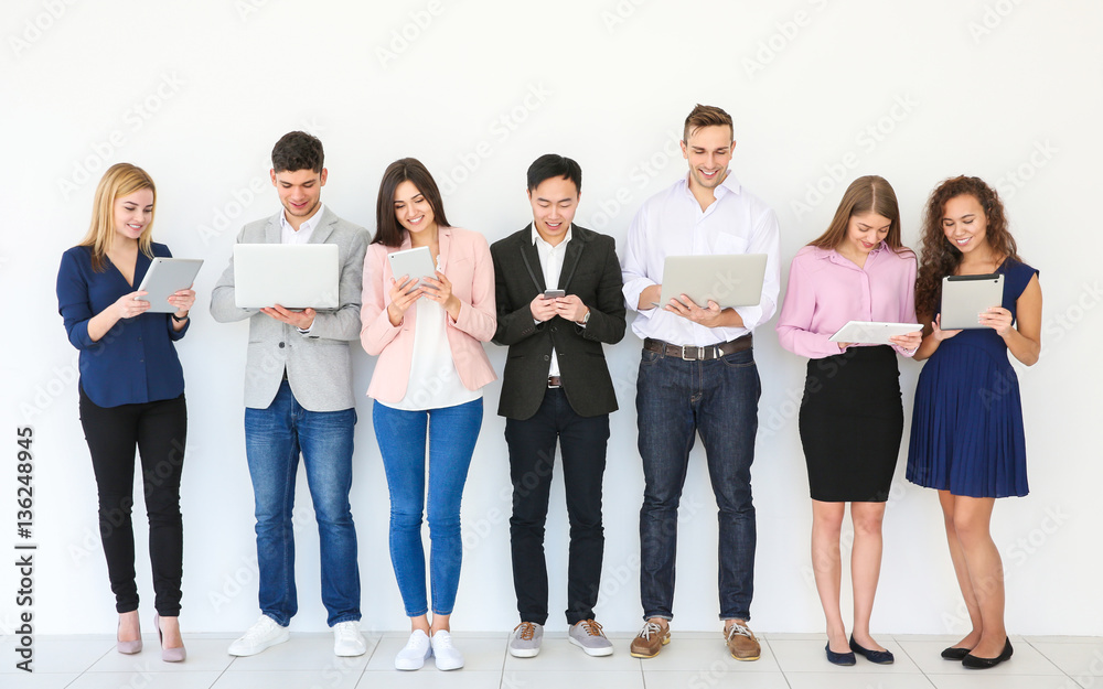 People with gadgets standing near light wall