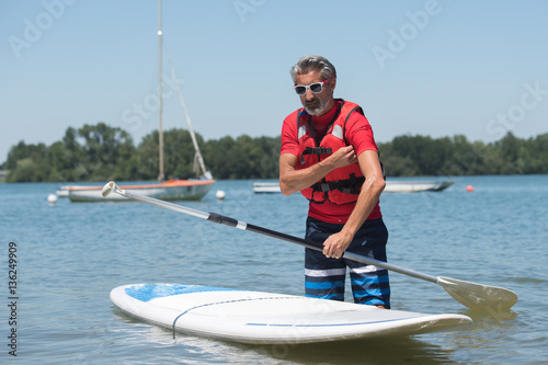 man next to a stand-up paddle board on the lake © auremar