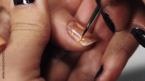 Female beautitian hand draw beige pattern on nail in beauty shop, close up white table photo