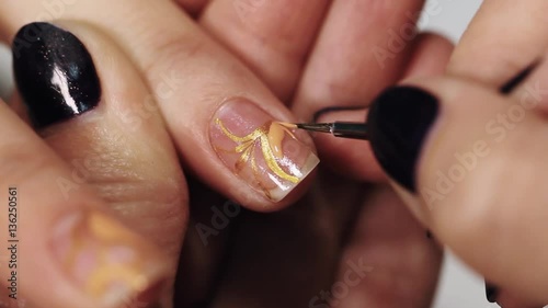 Woman beautitian hand draw beige pattern on nail in beauty saloon, close up white table photo