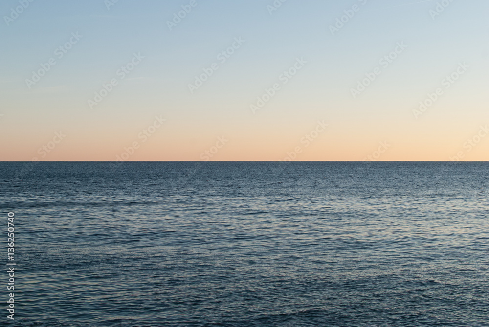 Open sea at sunset with colorful gradient sky background, horizon line splitting the photo in half