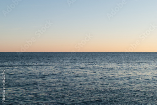 Open sea at sunset with colorful gradient sky background, horizon line splitting the photo in half