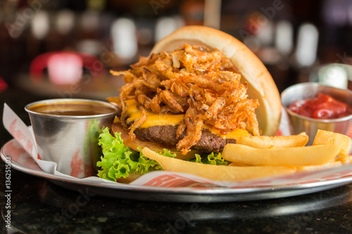 Fried onion rings burger with onion and tomatoes served with fries.