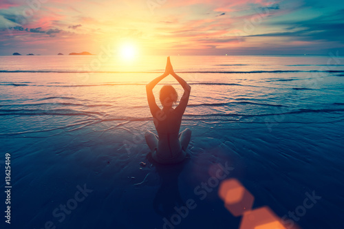 Silhouette yoga woman on the sea beach at sunset.