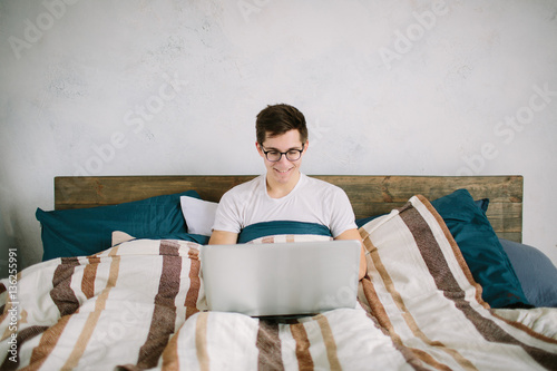 casual young man using laptop in bed at home photo