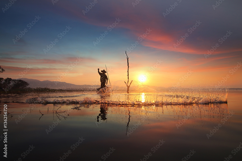 Silhouette of fishermen using nets to catch fish at the Bangpra lake with beautiful scenery of nature during sunrise time. Bang Pra Reservoir at Chonburi province in Thailand