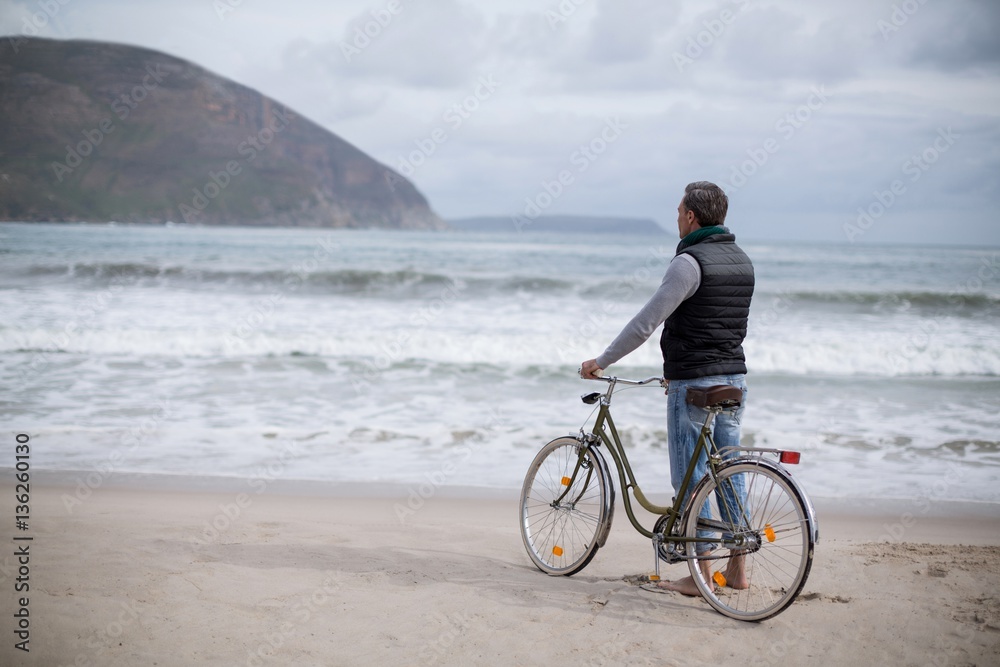 Mature man standing with bicycle on the beach 