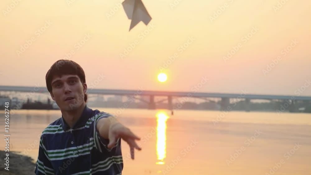 Young thoughtful guy launch paper plane against the sea during beautiful sunset with sun flare and reflections in the water in slowmotion, as in childhood. 1920x1080 Young thoughtful guy launch paper plane against the sea during beautiful sunset with sun flare and reflections in the water in slowmotion, as in childhood. 1920x1080