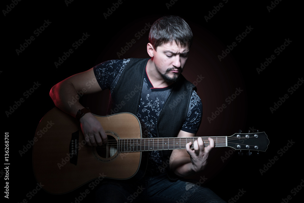 Obraz premium Portrait of a young bearded guitarist clamping chord on an acoustic guitar on a black background