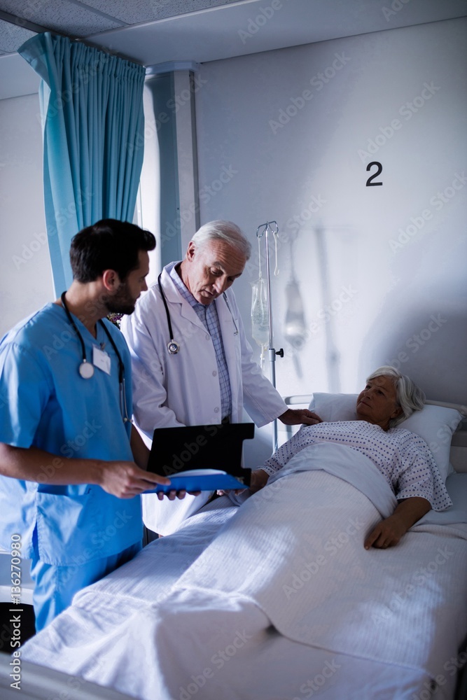 Doctors discussing a medical report with patient on bed Doctors discussing a medical report with patient on bed