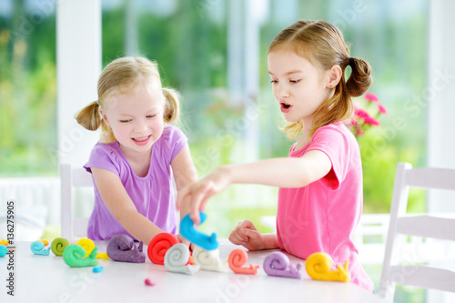 Two cute little sisters having fun together with modeling clay at a daycare. Creative kids molding at home. Children play with plasticine or dough.