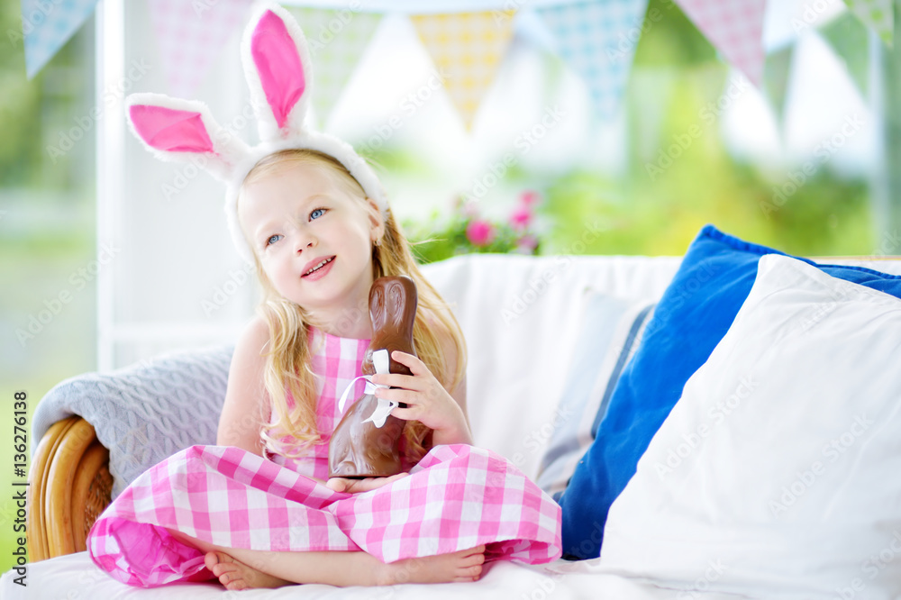 Cute little girl wearing bunny ears eating chocolate Easter rabbit Cute little girl wearing bunny ears eating chocolate Easter rabbit