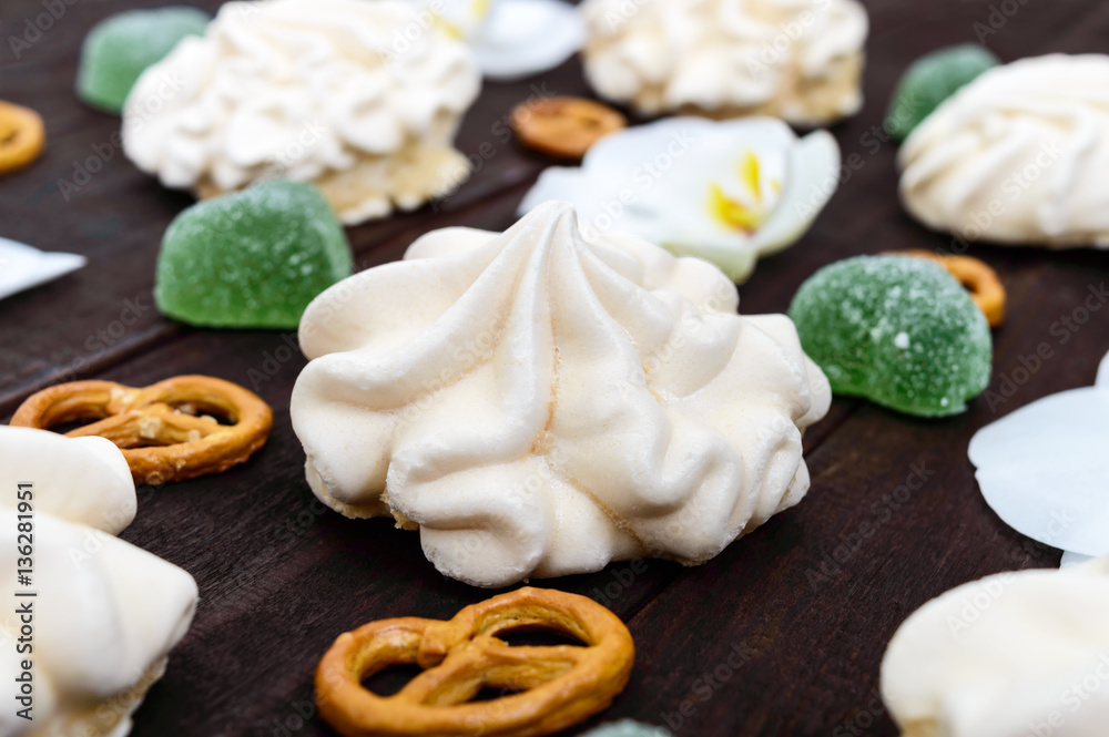 Sweets: meringues and jelly hearts, white orchid flowers, salty Bretzel on a dark wooden board.Close up