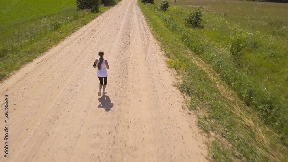Beautiful teenage girl running on the road on sunny summer day.Aerial view:young beautiful girl running and listening to music with headphones.4K video,ultra HD. Beautiful teenage girl running on the road on sunny summer day.Aerial view:young beautiful girl running and listening to music with headphones.4K video,ultra HD.