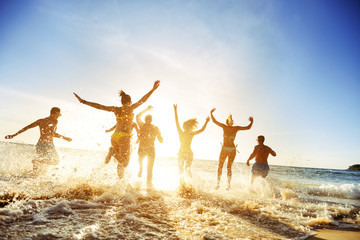 Group of happy young friends jumping into ocean at sunset, summer beach vacation
