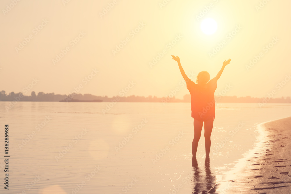 Girl teenager standing in the water with a raised hands at sunset