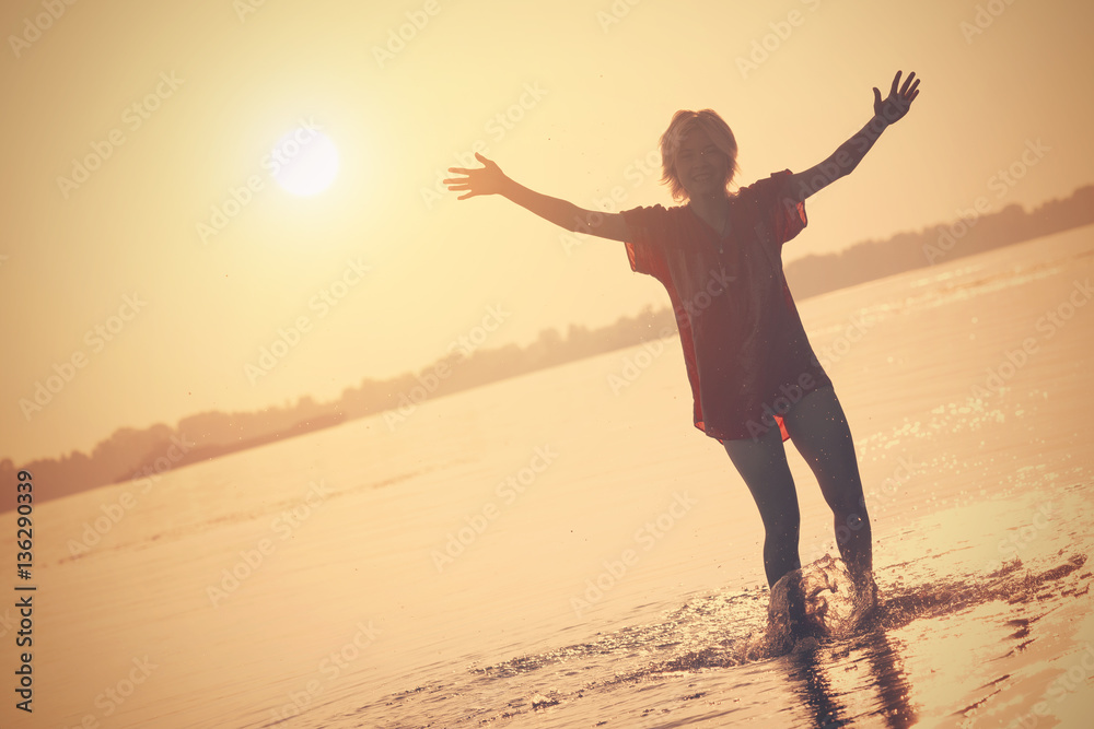 Girl teenager standing in the water with a raised hands at sunset