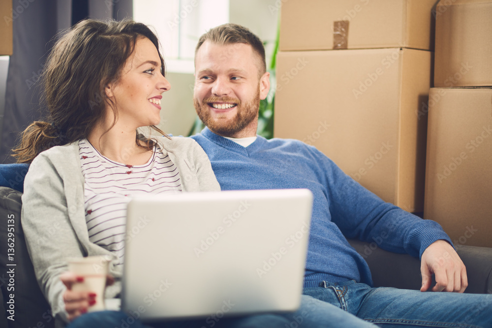couple in new apartment using laptop. Lot of moving boxes around them couple in new apartment using laptop. Lot of moving boxes around them